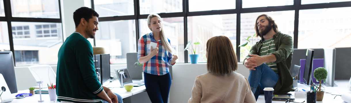 Four office mates talking while leaning on tables or wall